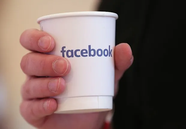 Mão segurando um copo de papel com o logotipo do Facebook